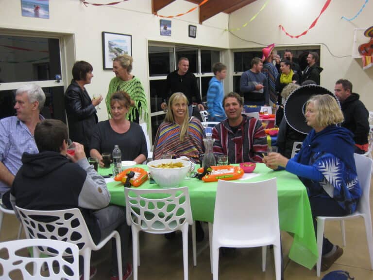 Celebration at Raglan Surf Lifesaving club, featuring members and supporters enjoying a social event with food, drinks, and festive decorations, highlighting community spirit and surf rescue dedication.