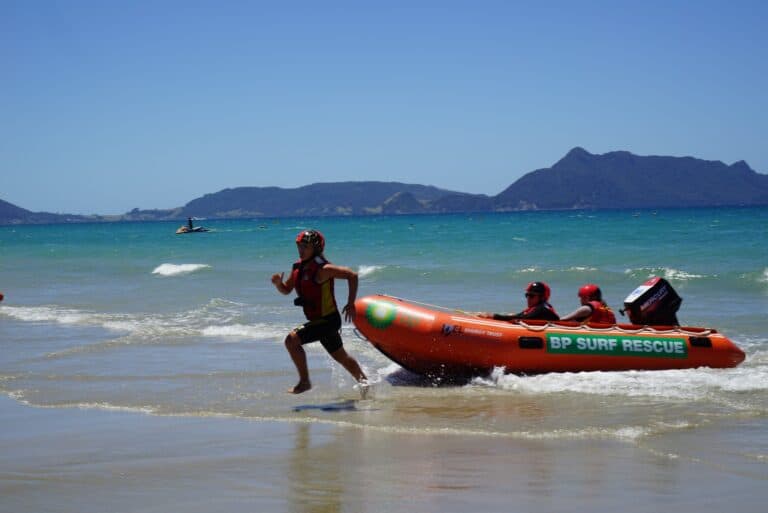 Raglan Surf Lifesaving rescue team practicing water rescue drills with inflatable rescue boat on the beach, high visibility gear, safety helmets, in New Zealand.